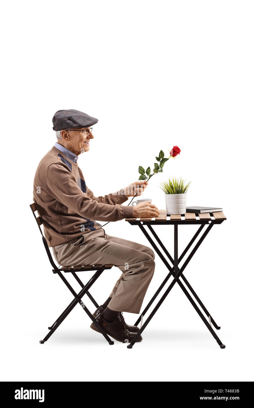 Full length profile shot of an elderly man sitting at a coffee table and holding a red rose isolated on white background Stock Photo