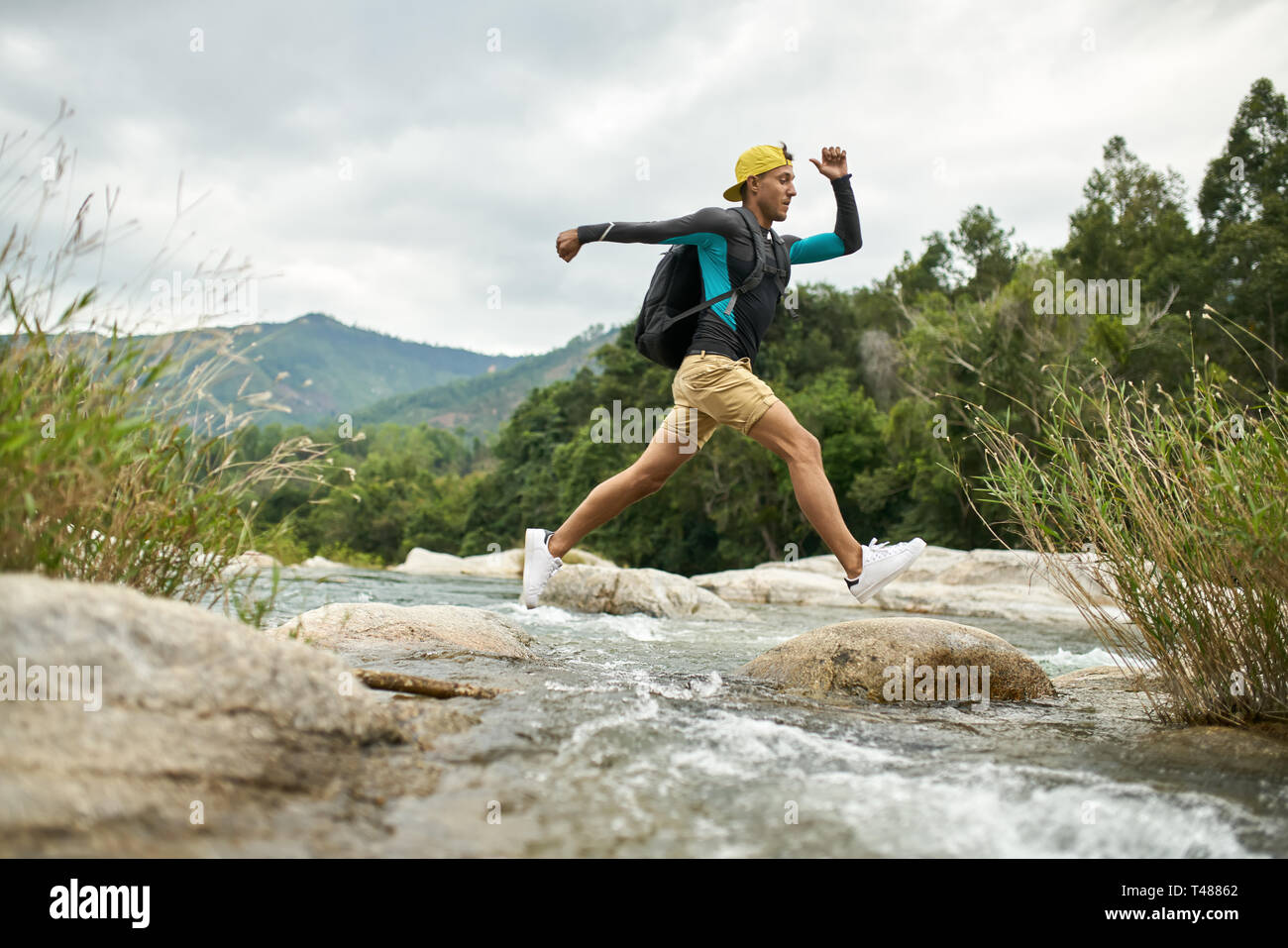Traveler running through shallow rocky river on nature background Stock Photo