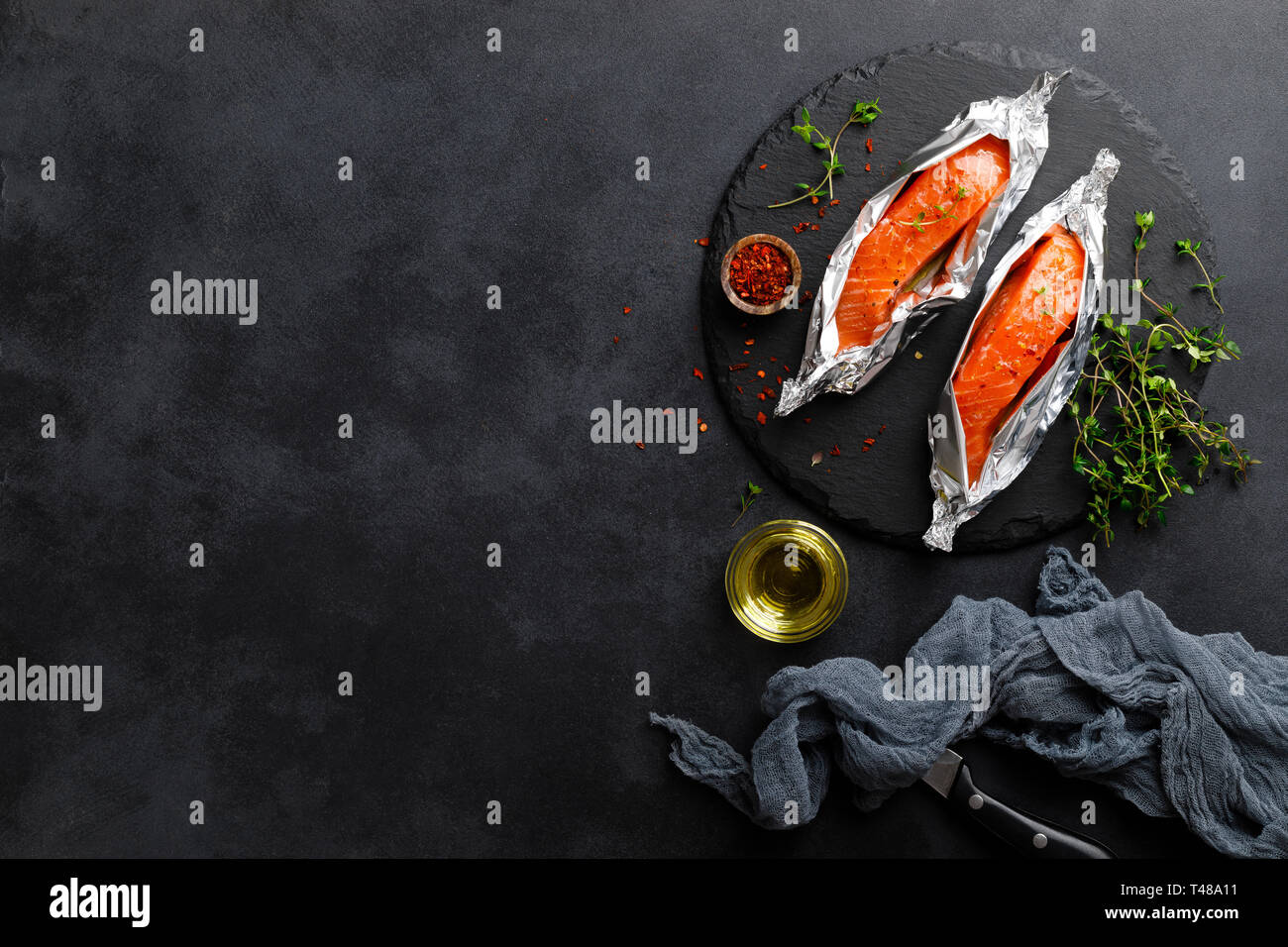 Raw salmon fish fillet in foil on black background Stock Photo - Alamy