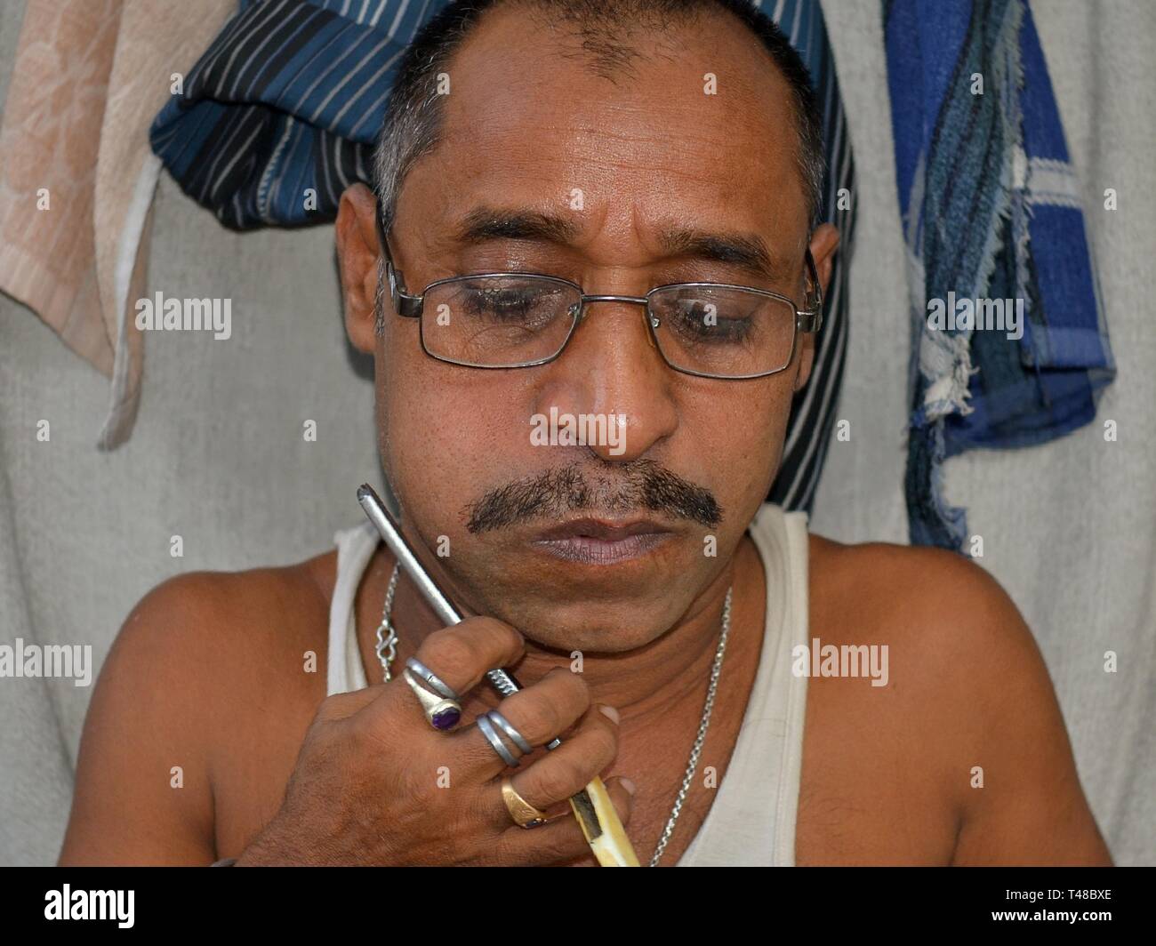 Funny Indian curbside barber with puffed up cheeks trims his menjou moustache with a straight razor. Stock Photo