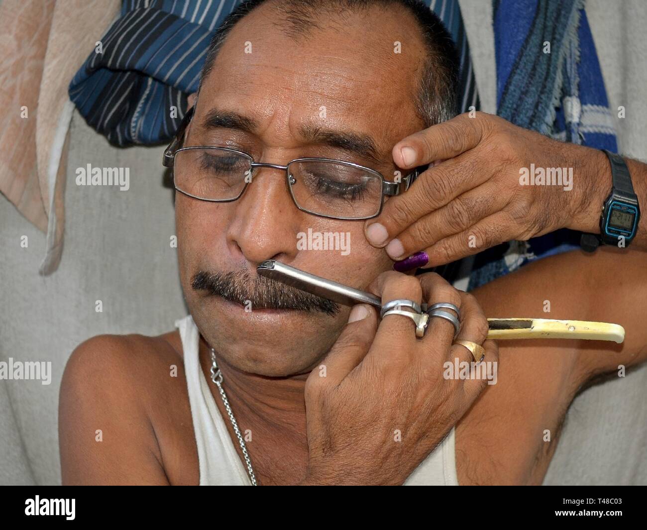 Funny Indian curbside barber with puffed up cheeks trims his ...