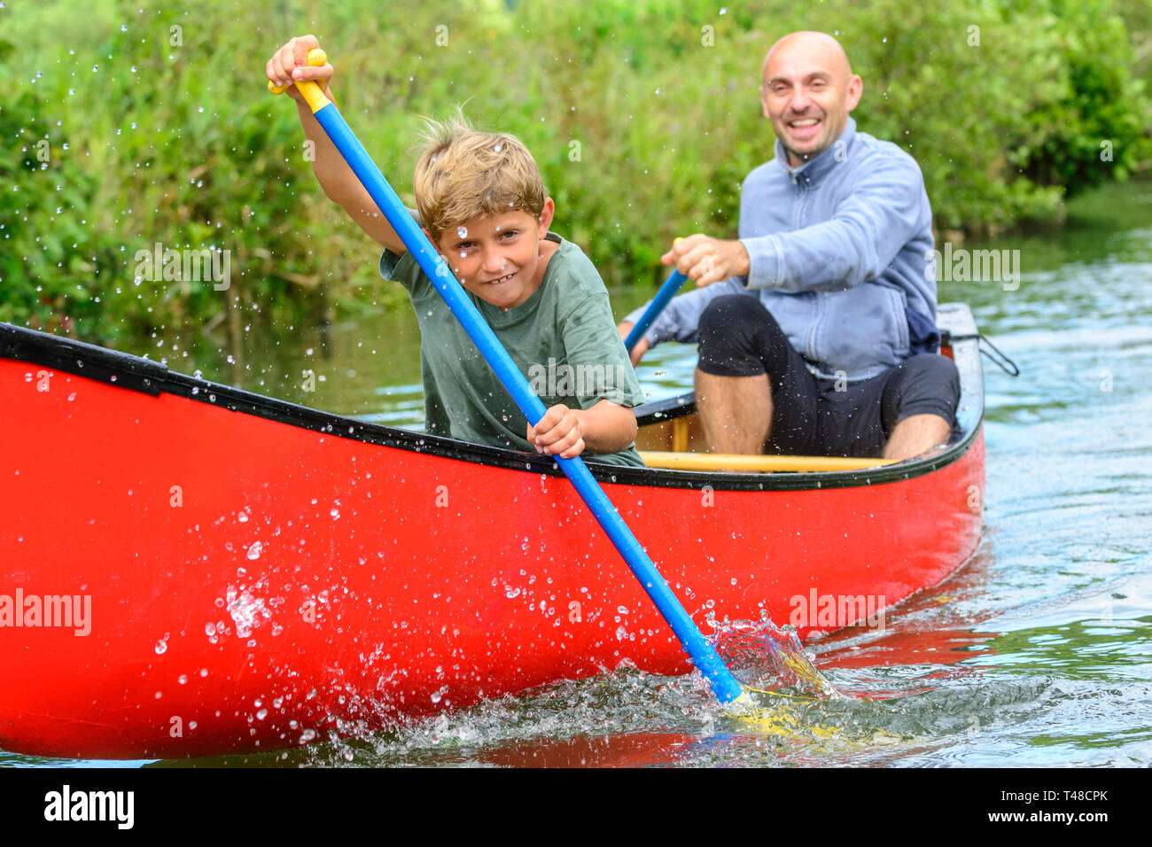 Young boy paddling eagerly with his father in canoe Stock Photo