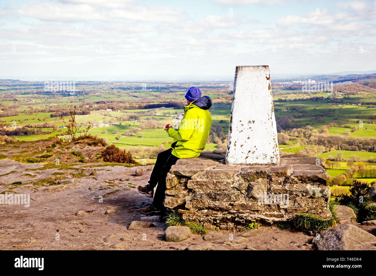 Man sitting enjoying the view over the Cheshire plain from the trig point on top of Bosley cloud or Cloud End near Congleton in Cheshire Stock Photo