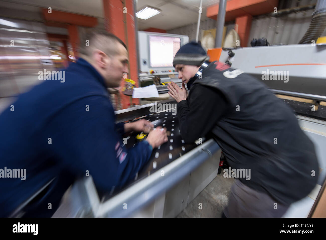 two young carpenters calculating and programming a cnc wood working machine in workshop. wood workers preparing a computer program for CNC machine at  Stock Photo