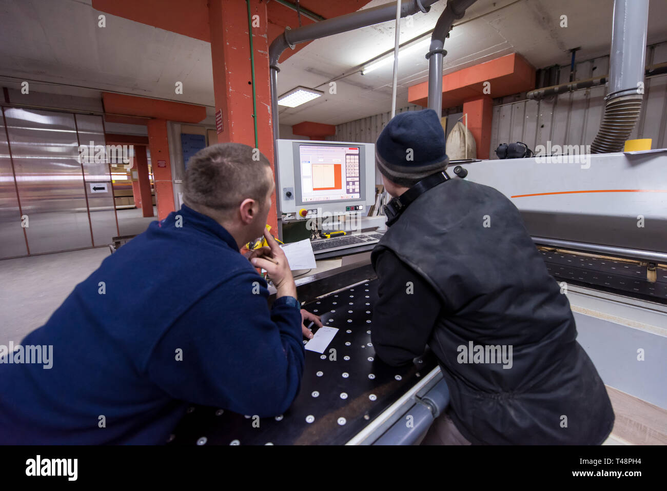 two young carpenters calculating and programming a cnc wood working machine in workshop. wood workers preparing a computer program for CNC machine at  Stock Photo