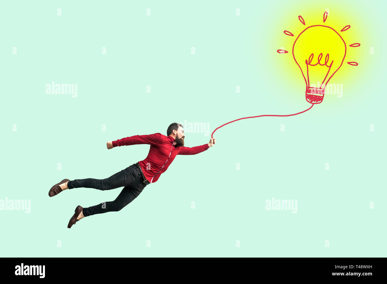 Young successful businessman flying with his perfect idea. funny young successful bearded man in red shirt holding drawed bulb lamp and flying. indoor Stock Photo