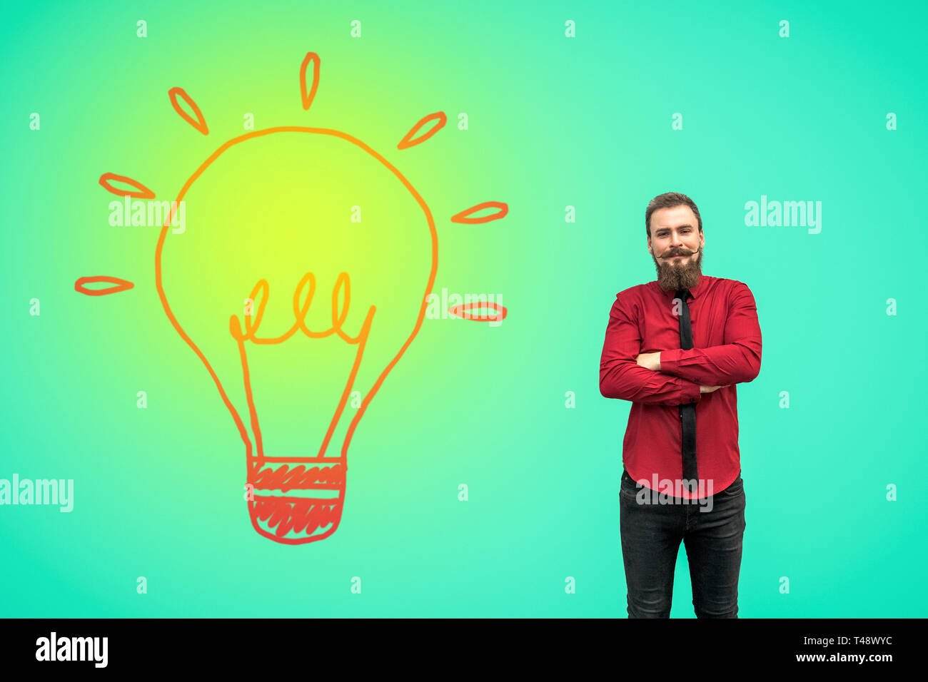 Portrait of handsome satisfied bearded businessman in red shirt standing with raised arms and and looking at camera and smiling near turned on big bul Stock Photo