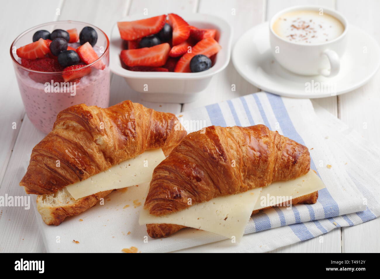 French breakfast: croissant sandwich with cheese, fruit salad, chia seeds yogurt, and a cup of cappiccino Stock Photo