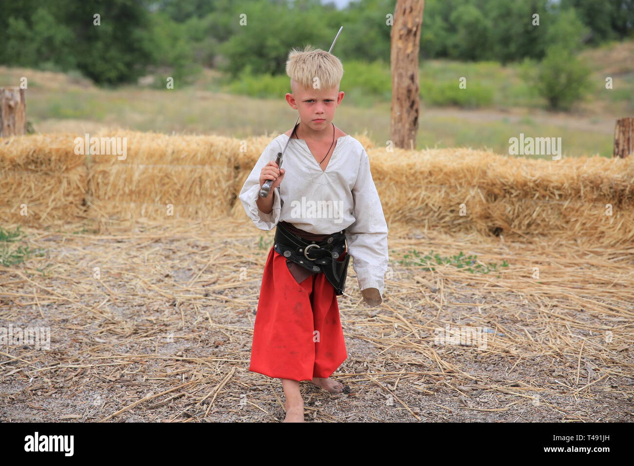 KHORTYTSIA, UKRAINE - JULY 03, 2018: Young boy Ukrainian Cossack with saber in Zaporozhian Sich. It was inhabited by Cossacks who lived beyond the rap Stock Photo