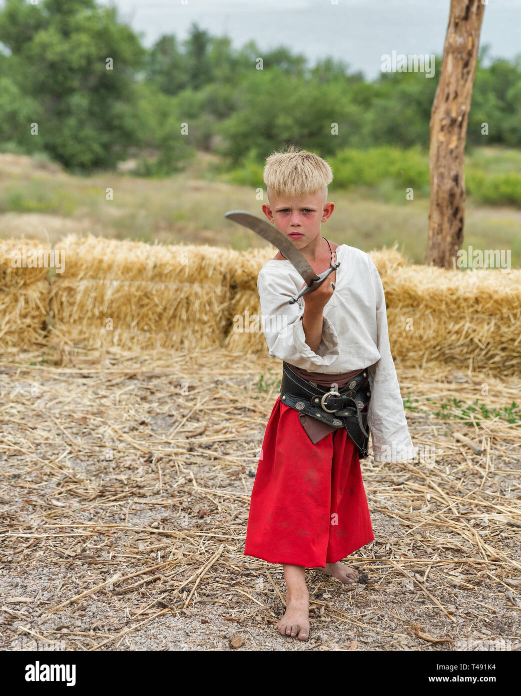 KHORTYTSIA, UKRAINE - JULY 03, 2018: Young boy Ukrainian Cossack with saber in Zaporozhian Sich. It was inhabited by Cossacks who lived beyond the rap Stock Photo