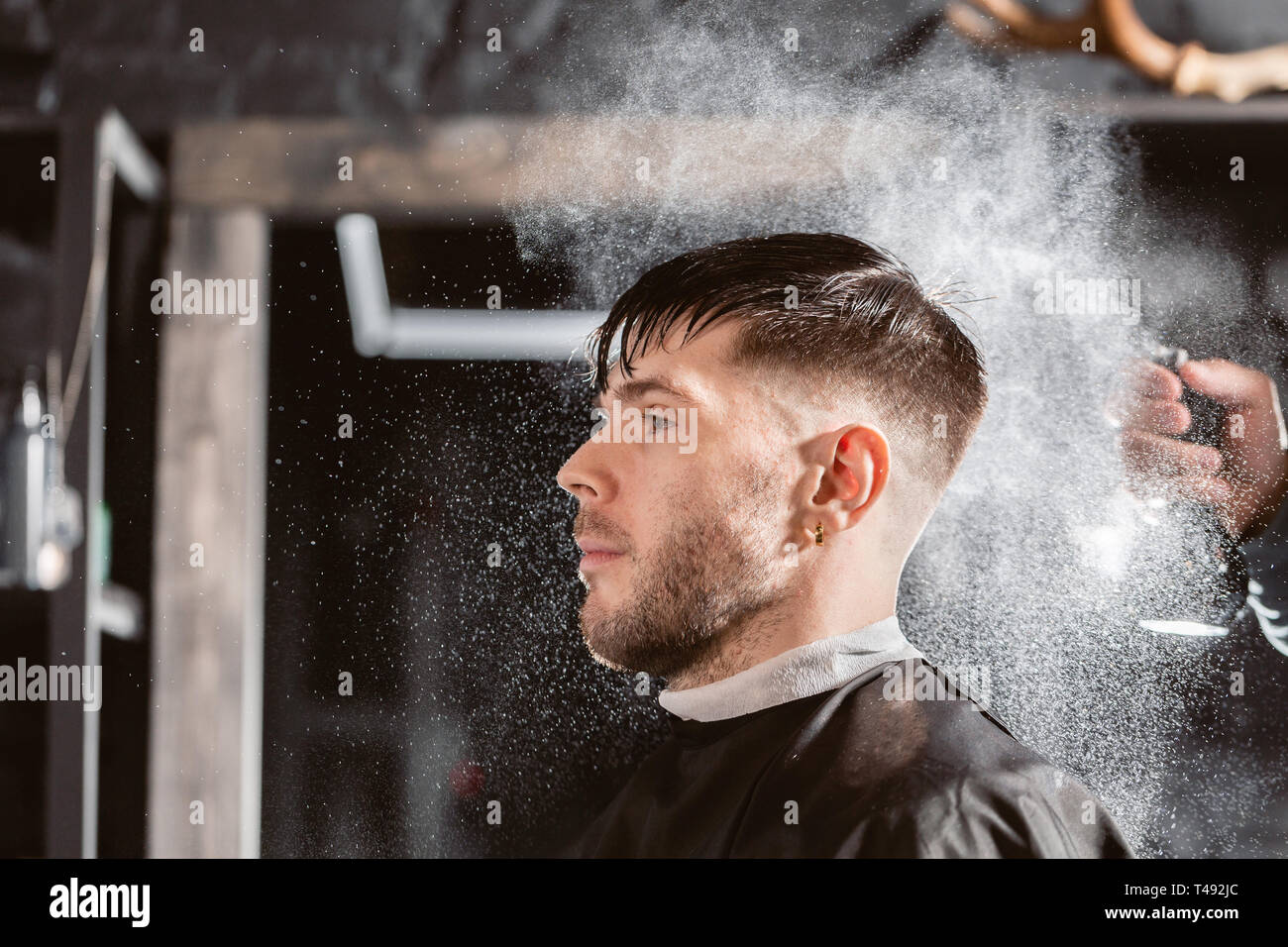Barber sprays clean water on head in barbershop. Professional trimmer tool  cuts beard and hair on young guy in barber shop salon Stock Photo - Alamy