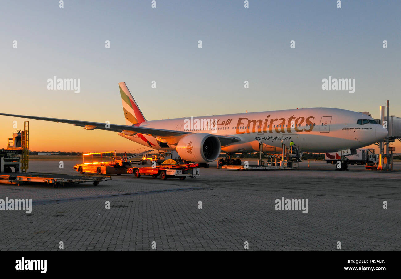 A sunset full view of an Emirates Boeing 777 at the gate, being