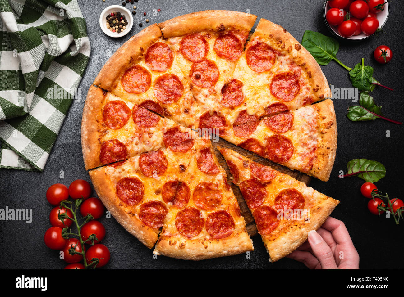 Pepperoni pizza on a black concrete background. Hand picking slice of pepperoni pizza. Table top view. Party food, fast food concept Stock Photo