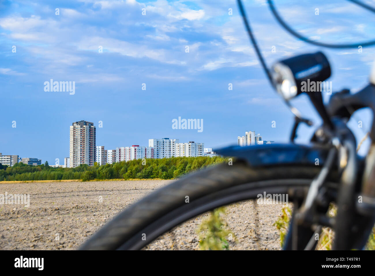 View over the unfocused front wheel of a bicycle across a field to the satellite town of Gropiusstadt in Berlin-Neukölln. Stock Photo