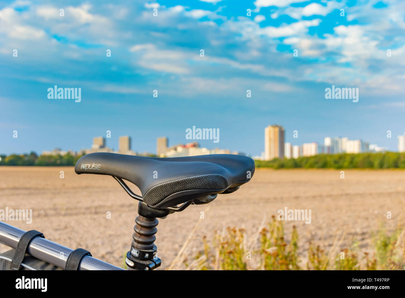 Berlin, Germany - September 12, 2018: View over the saddle of a bicycle. In the background you can see a field and a unfocussed satellite town. Stock Photo