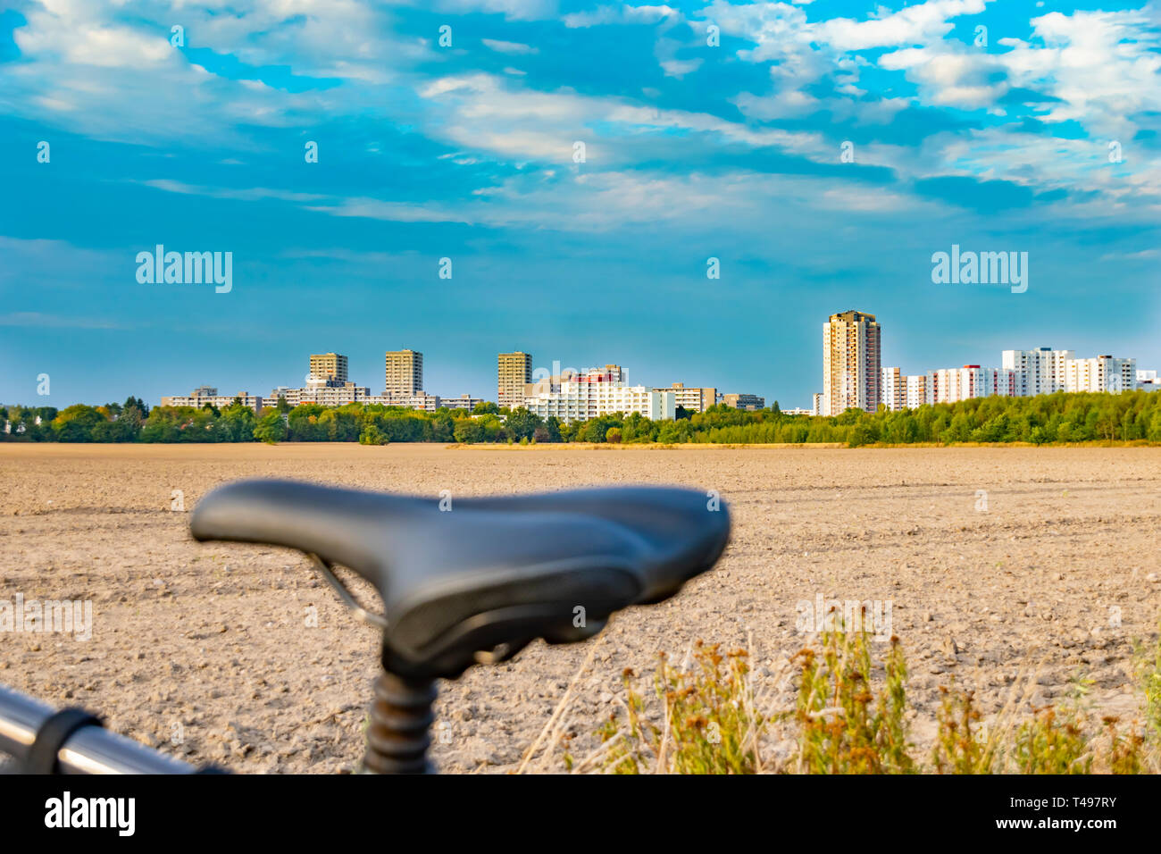 View over the saddle of a bicycle. In the background you can see a field and the unfocussed satellite town of Gropiusstadt in Berlin-Neukölln. Stock Photo