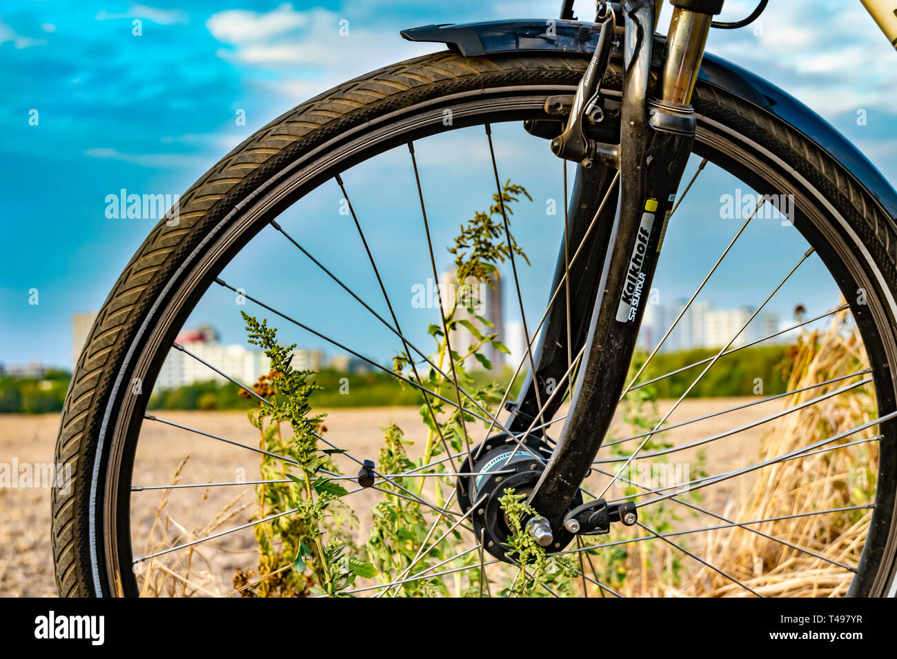 Berlin, Germany - September 12, 2018: View through the front wheel of a bicycle. In the background you see a field and a unfocussed satellite town. Stock Photo