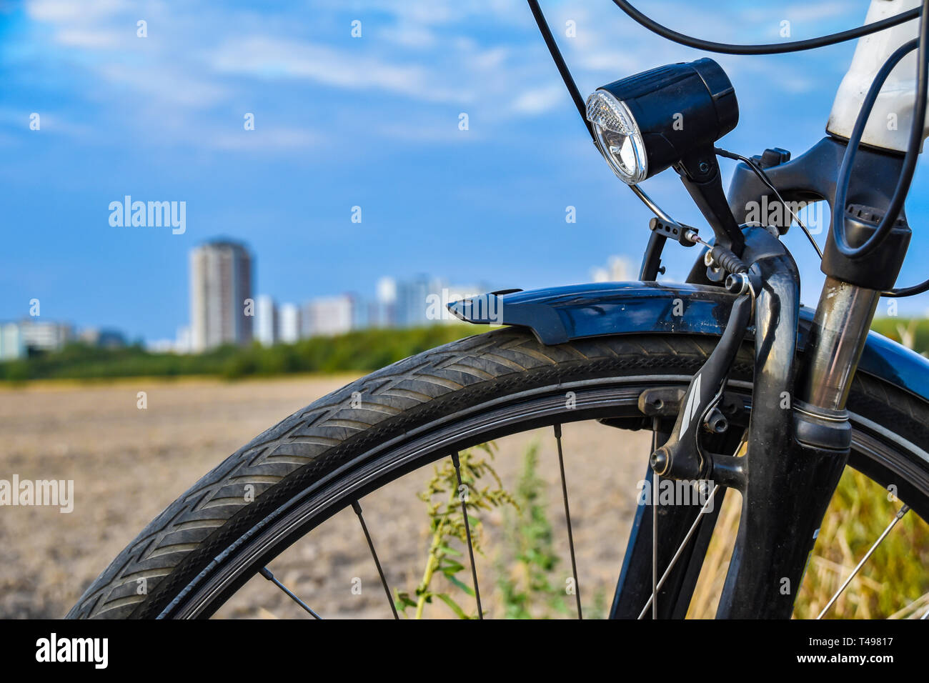 View over the front wheel of a bicycle. In the background you can see a field and the unfocussed satellite town of Gropiusstadt in Berlin-Neukölln. Stock Photo