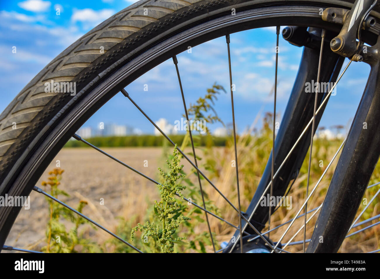 View through the front wheel of a bicycle. In the background you can see a field and the unfocussed satellite town of Gropiusstadt in Berlin-Neukölln. Stock Photo