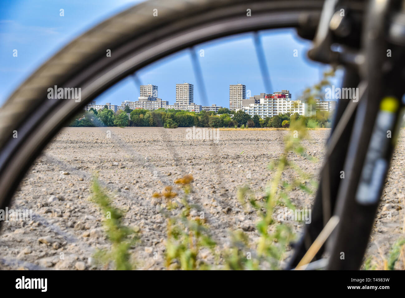 View through the unfocused front wheel of a bicycle across a field to the satellite town of Gropiusstadt in Berlin-Neukölln. Stock Photo