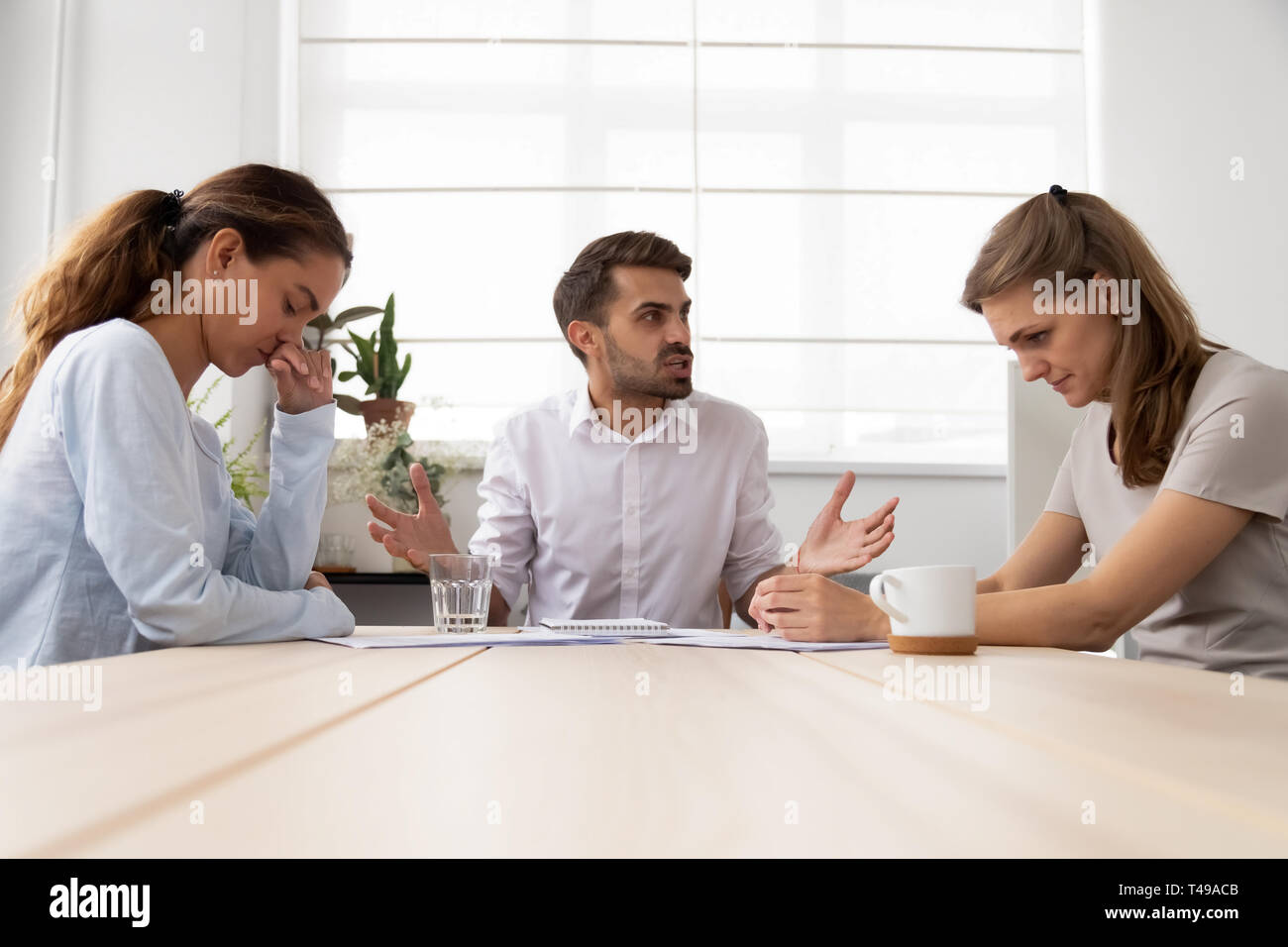 Angry mean male boss shouting criticizing stressed sad female employees Stock Photo