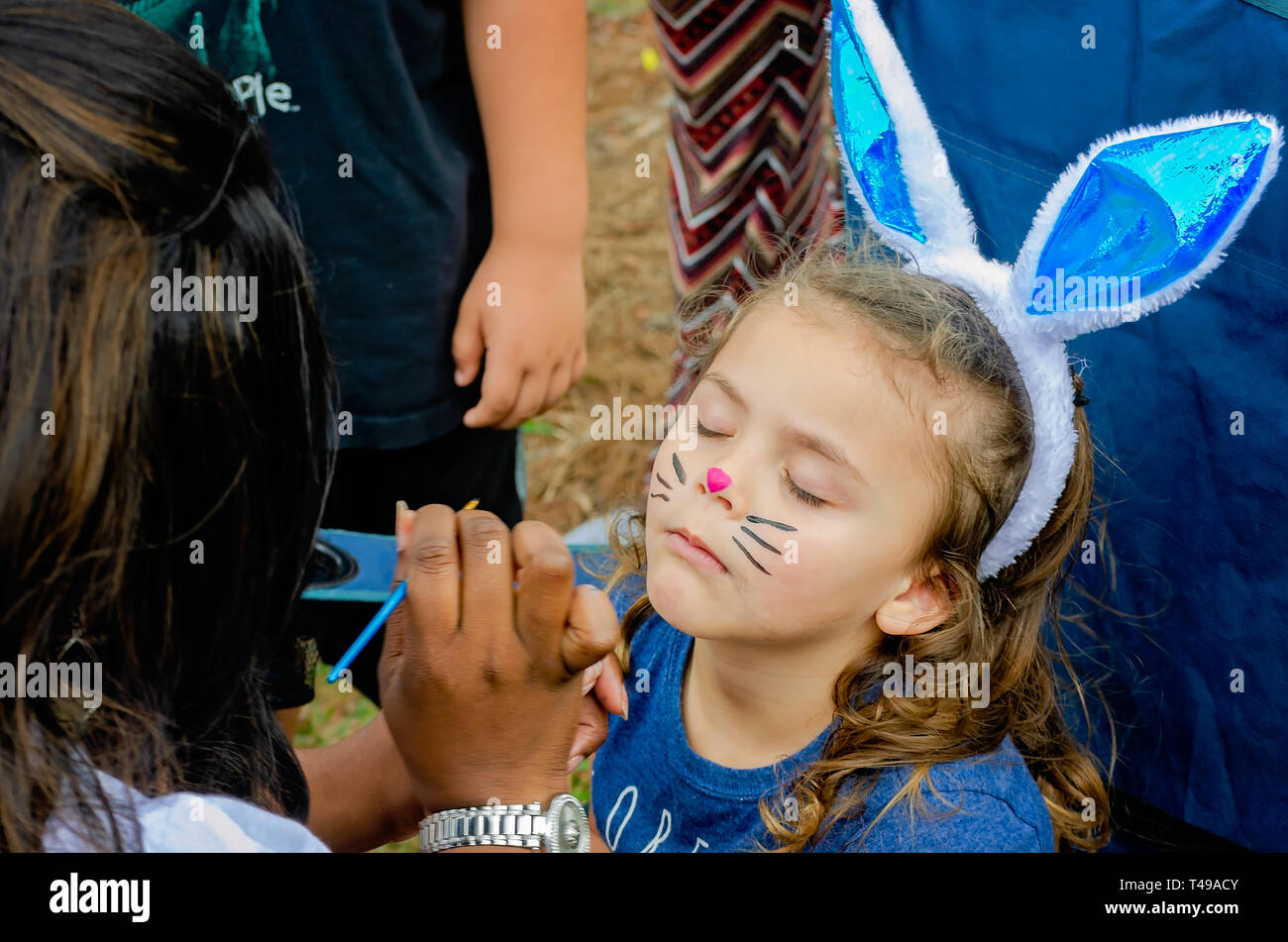 A girl closes her eyes as she gets her face painted during a community Easter egg hunt at Langan Park, April 13, 2019, in Mobile, Alabama. Stock Photo