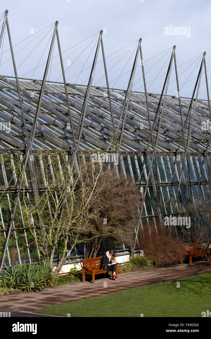 Young woman reading a boot outside a greenhouse at the Royal Botanic Garden in Edinburgh, Scotland, United Kingdom Stock Photo