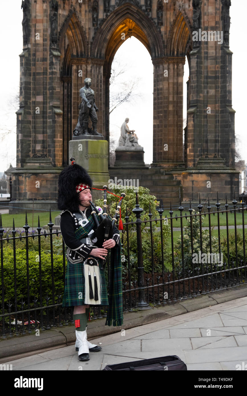 Scottish man wearing a kilt and playing the bagpipes in front of the Scott Monument to author Sir Walter Scott, Edinburgh, Scotland Stock Photo