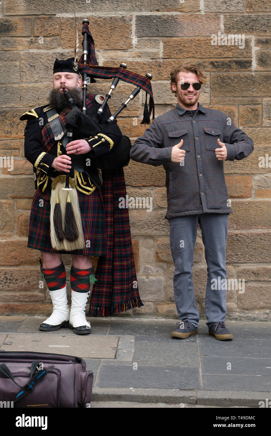 Tourist posing for a photograph next to a man playing the bagpipes while wearing a traditional scottish kilt Stock Photo