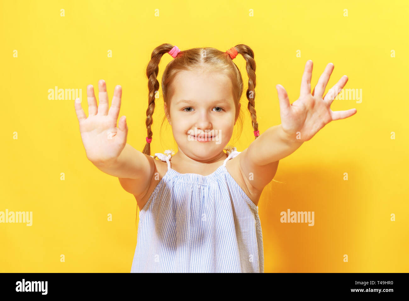 Portrait of a funny little girl on a yellow background. Preschool child shows palm. Stock Photo
