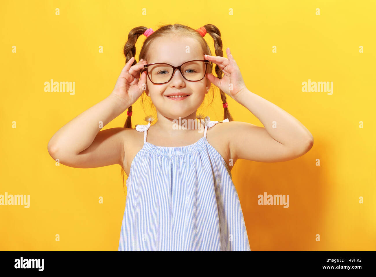 Portrait of a funny little girl on a yellow background. Preschool child straightens glasses. Stock Photo