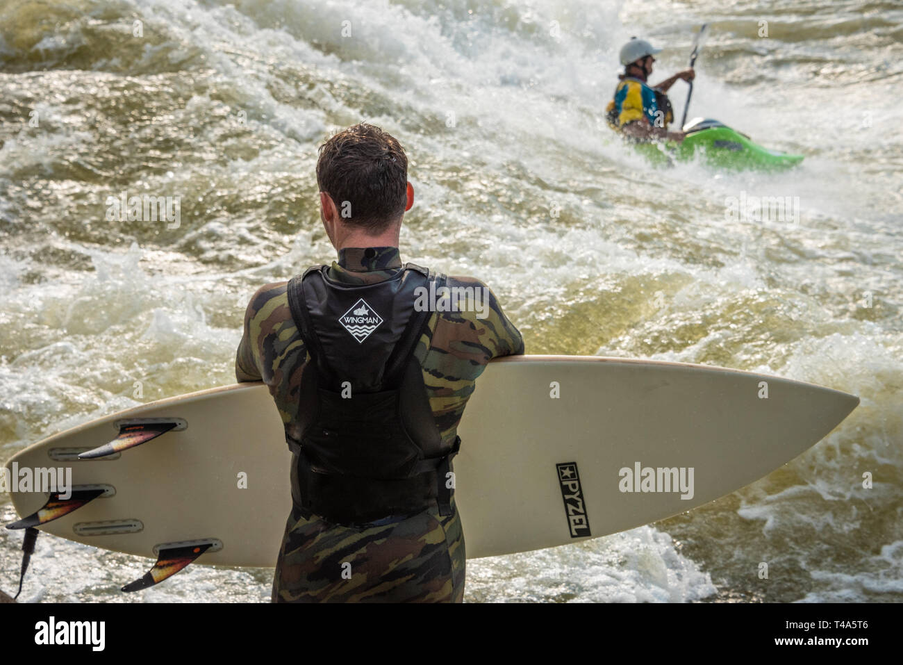 River surfer waits his turn as a freestyle kayaker rides the whitewater of the Good Wave on the Chattahoochee River in Columbus, Georgia. (USA) Stock Photo