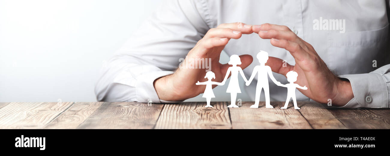 Man With Dress Shirt Holding His Protecting Hands Over His Paper Family / Family Protection And Care Or Adoption and Foster Care Concept. Stock Photo