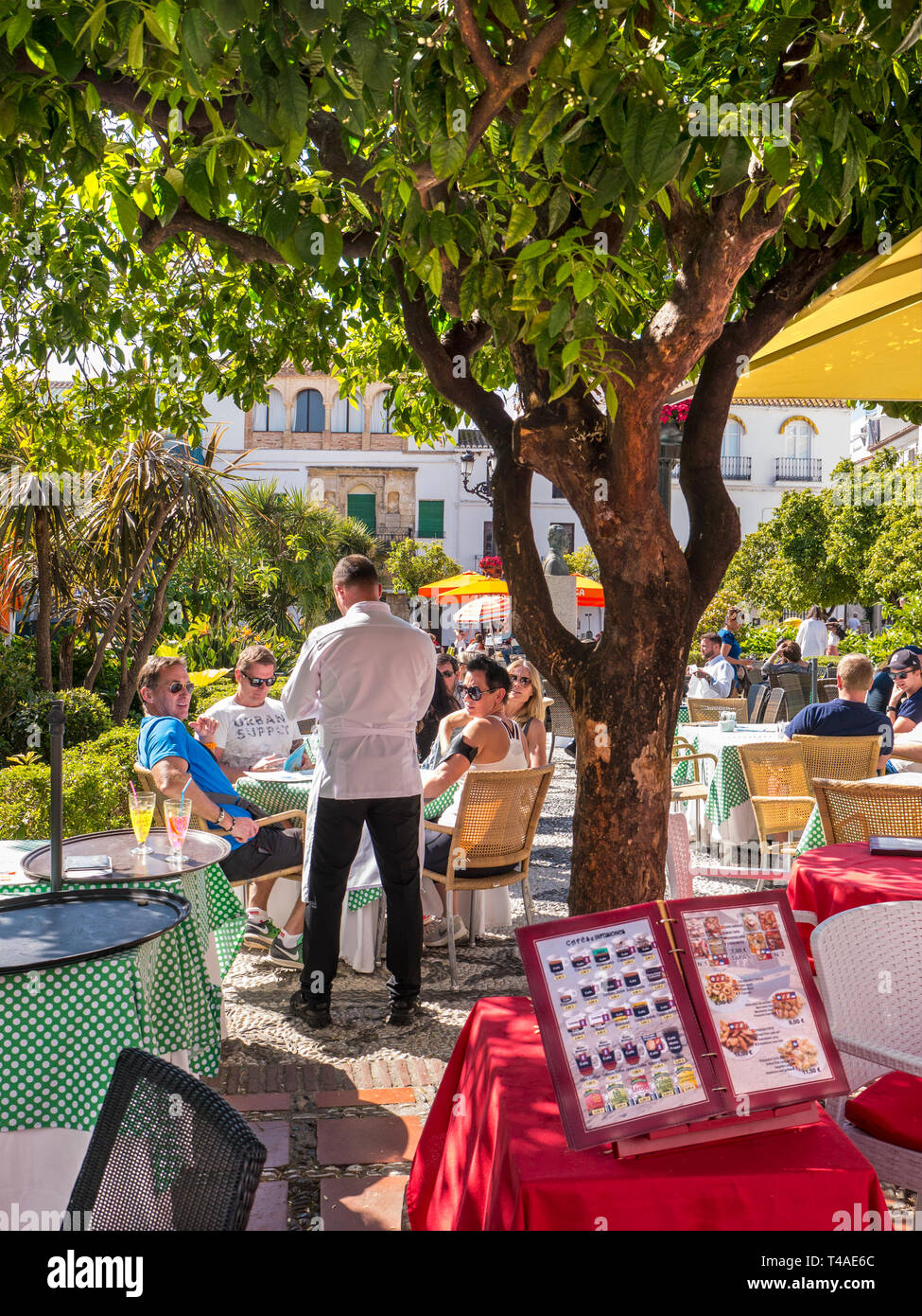 Alfresco dining, waiter taking order with illustrated menu in foreground.  Marbella Orange Square - Plaza de los Naranjos,  Old Town Marbella Spain Stock Photo