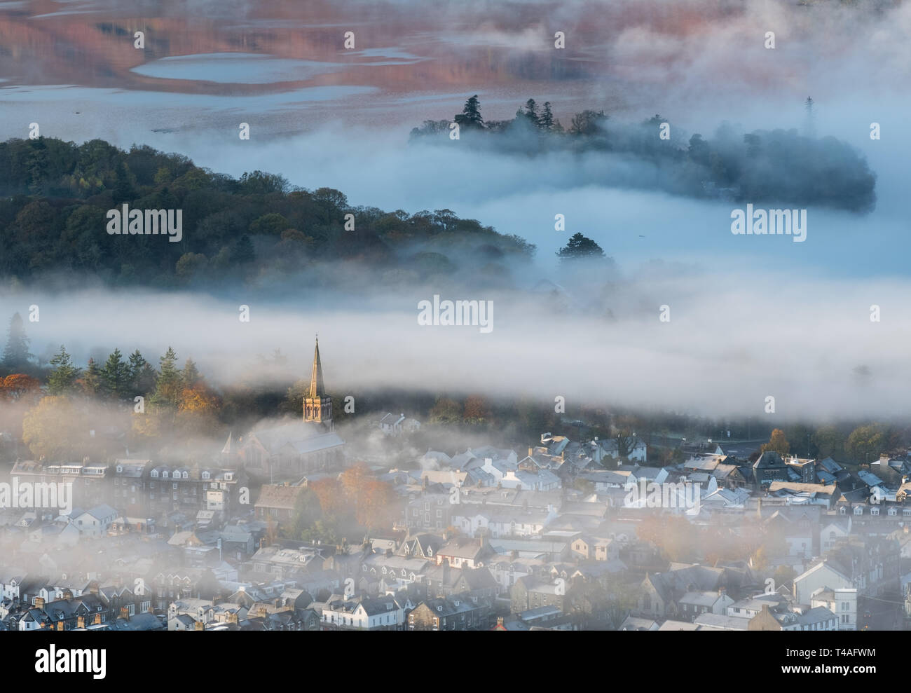 morning mist over derwentwater in the lake district.just for a brief moment the mist cleared around the church & the rising sun lit up the steeple ,i  Stock Photo