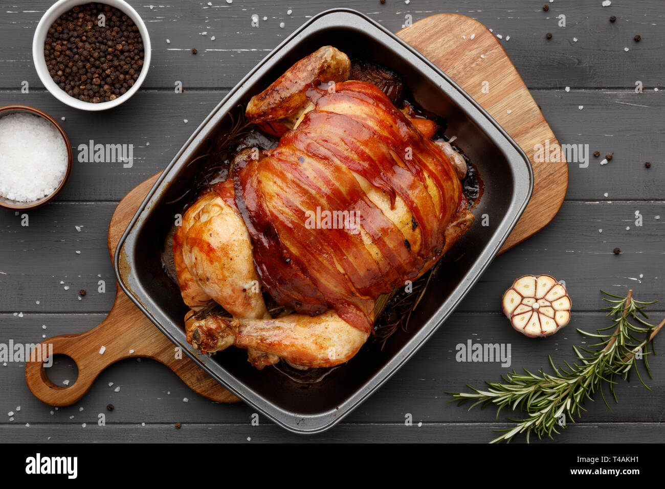roast chicken in a rasting tin with ingredients on a dark grey wooden
