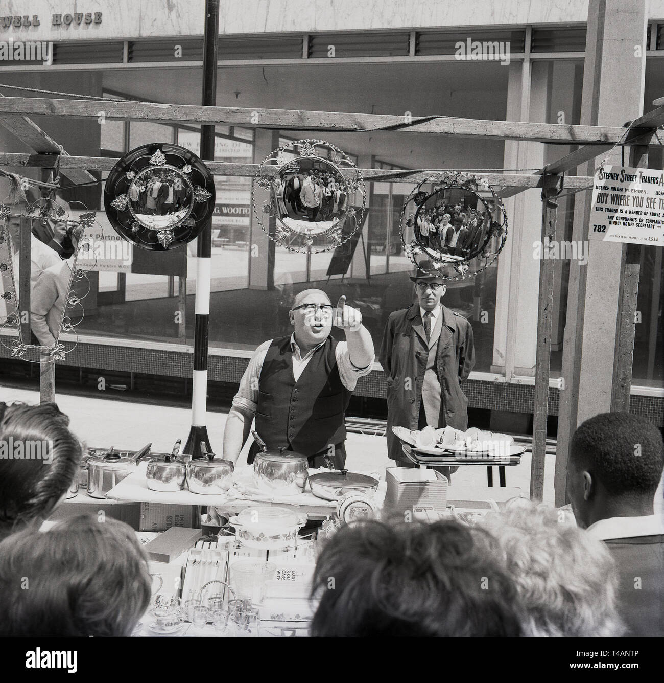 1960s, historical, street seller at his open-air stall sellling household wares, Stepney, East London, London, England, UK. Sign hanging says 'Stepney Street Traders Association' with the licence holder of the stall a M. Emden. Stock Photo