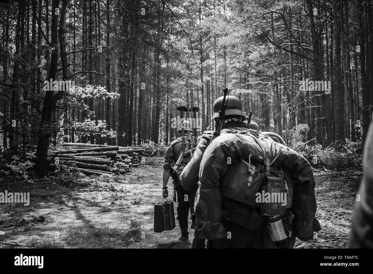 Re-enactors Dressed As German Infantry Soldiers In World War II Marching Walking Along Forest Road In Summer Day. Photo In Black And White Colors. Stock Photo