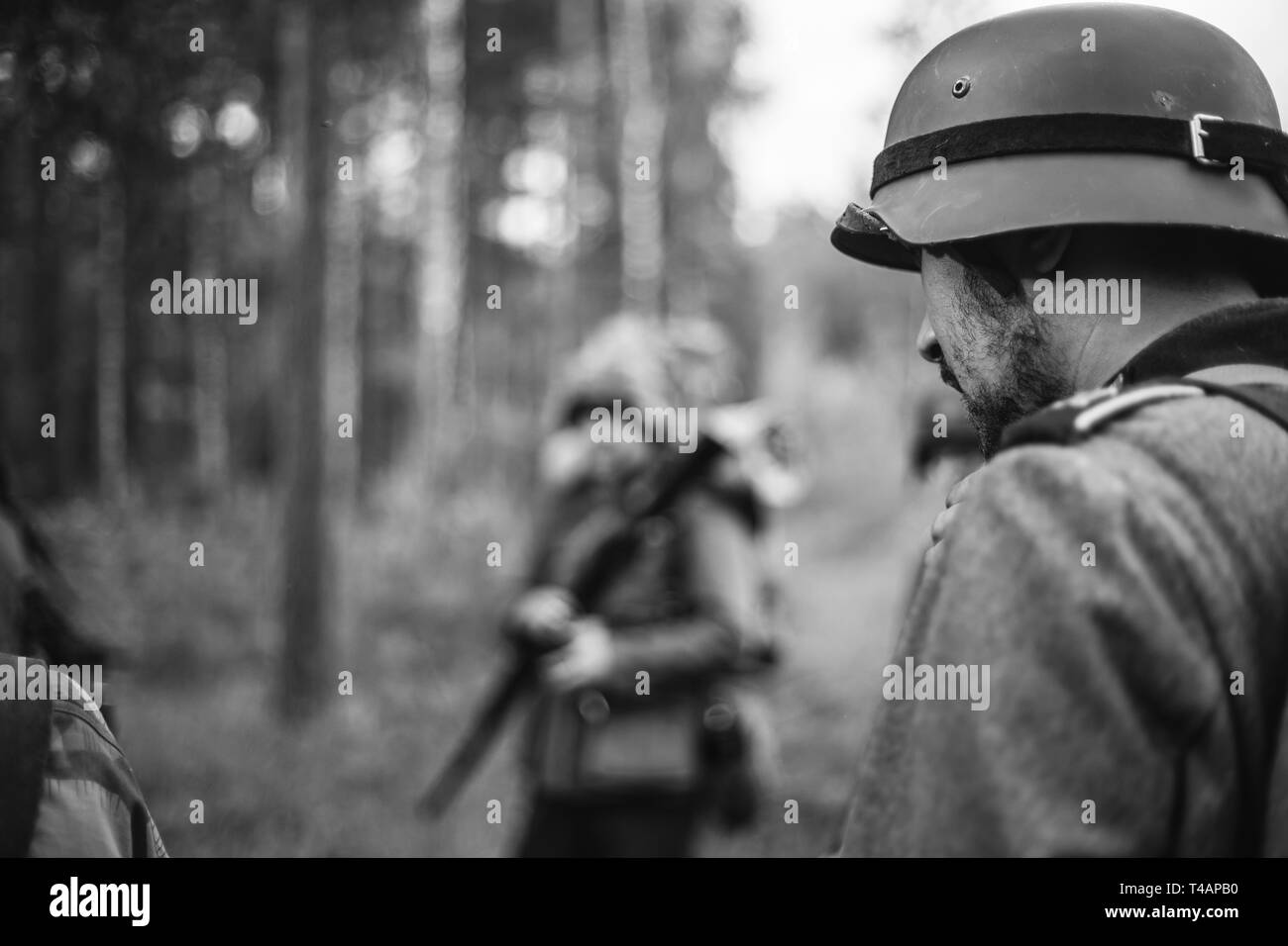 Re-enactors Dressed As World War II German Wehrmacht Soldiers Marching Walking Along Forest Road In Summer Day. Photo In Black And White Colors. Milit Stock Photo