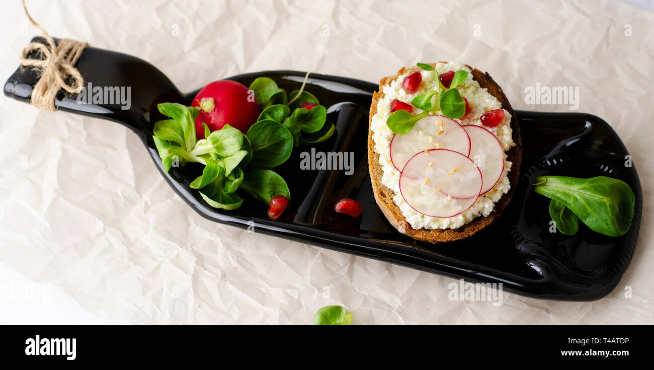 Toasts with cottage cheese and smashed avocado, radish, corn salad plant and pomegranate seeds on a serving bottle-plate. Top view. Copy space. Health Stock Photo