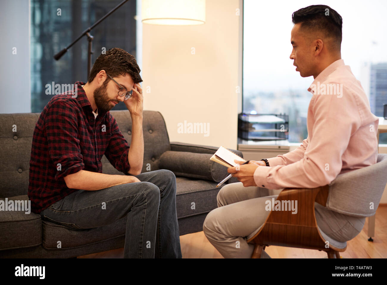 Unhappy Man Sitting On Couch Meeting With Male Counsellor In Office Stock Photo