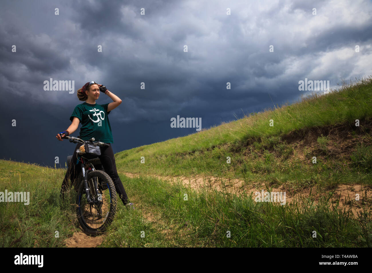 Brave, young girl on a bike outdoors on the background of the thunderhead front. She is in outdoors in stormy weather. Girl smiling Stock Photo
