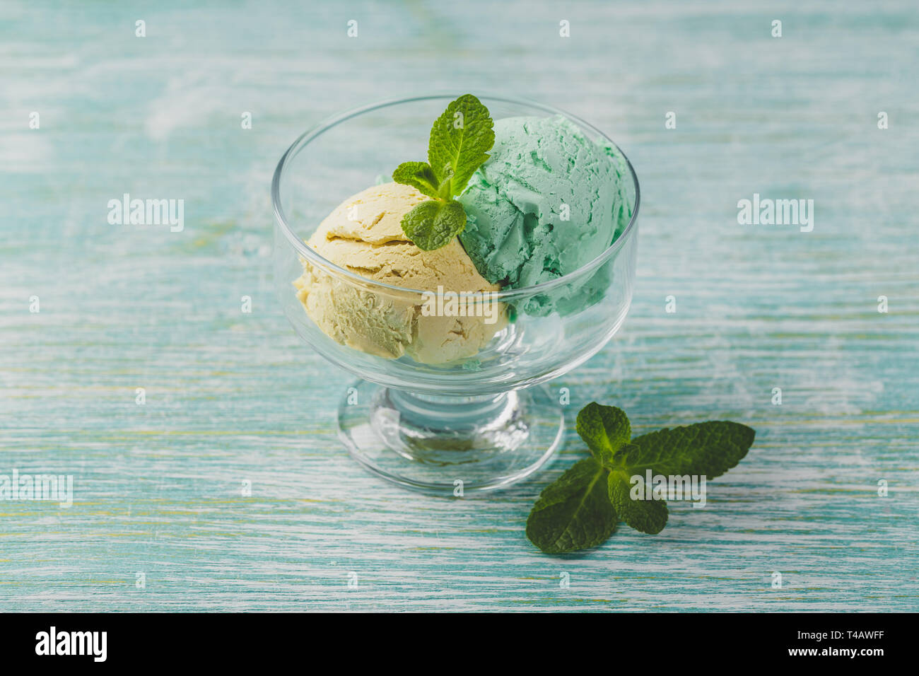Mint and lemon ice cream with mint leaves in glass bowl on green wooden background Stock Photo