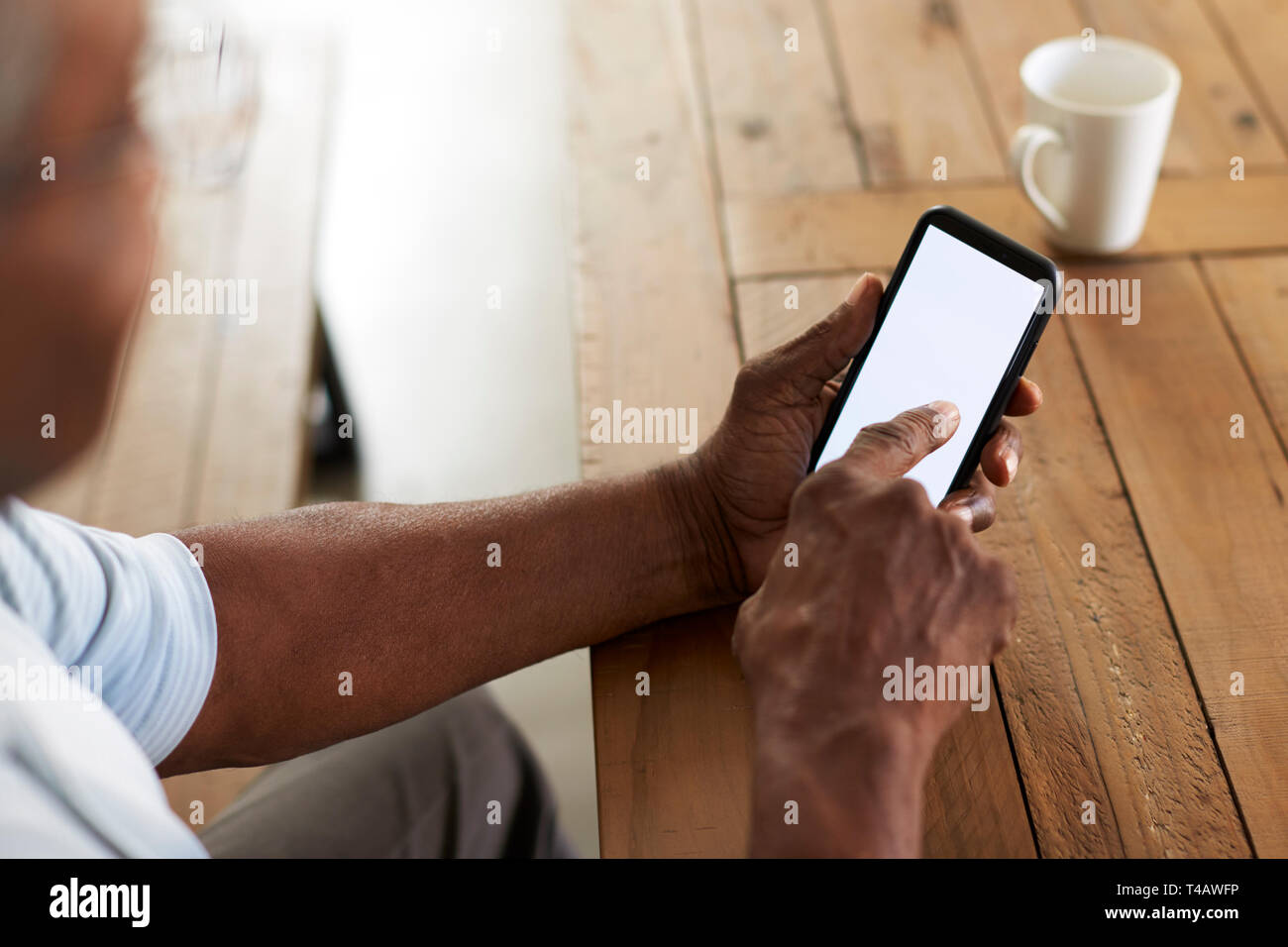 Senior black man sitting at a table using smartphone, over shoulder view Stock Photo