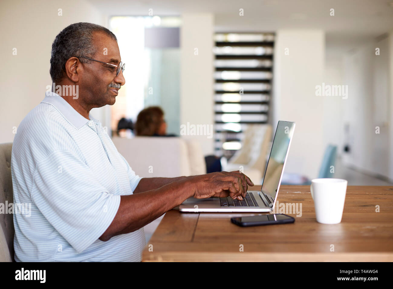 Senior black man sitting at the table using a laptop computer at home, side view Stock Photo