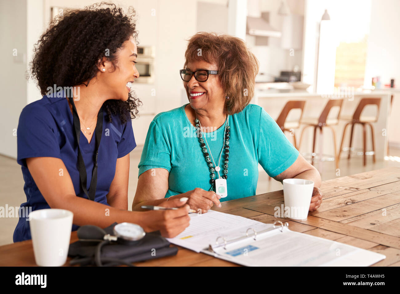 Female healthcare worker sitting at table smiling with a senior woman during a home health visit Stock Photo