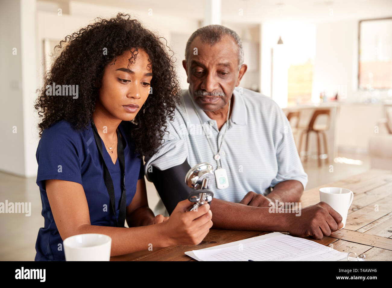 Female healthcare worker checking the blood pressure of a senior man during a home visit Stock Photo
