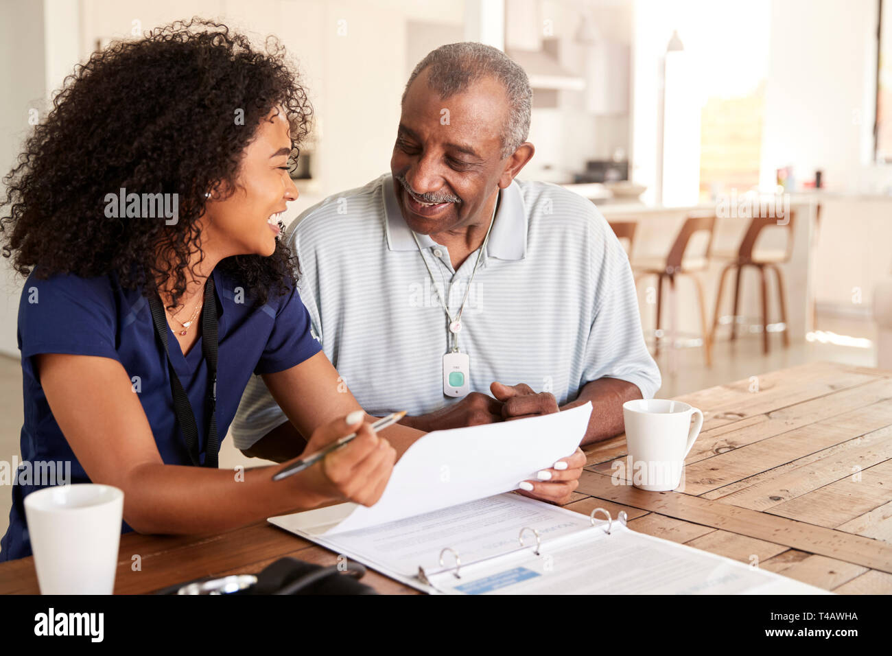 Happy female healthcare worker sitting at table smiling with a senior man during a home health visit Stock Photo