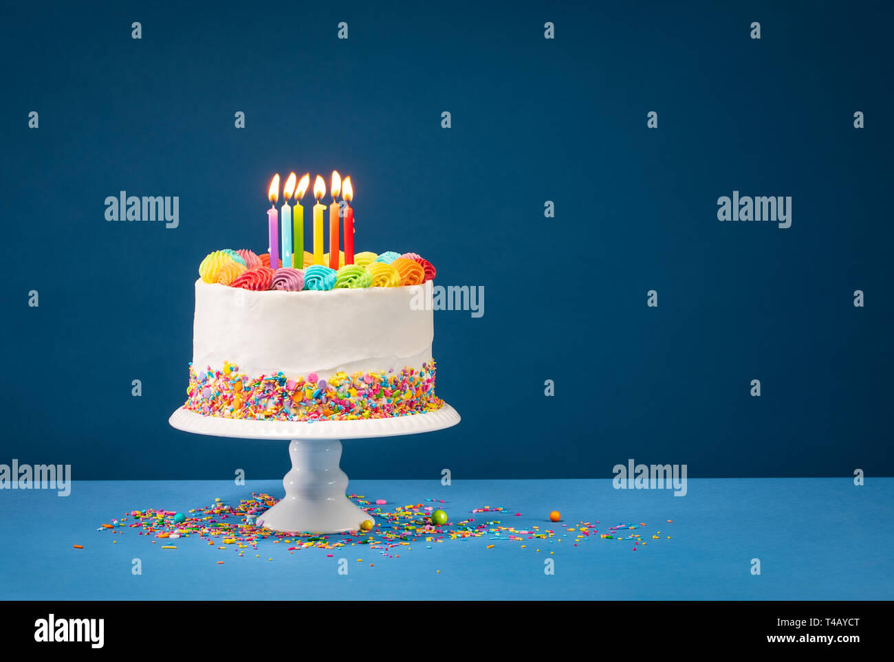 Birthday cake with rainbow icing, colourful Sprinkles and lit candles