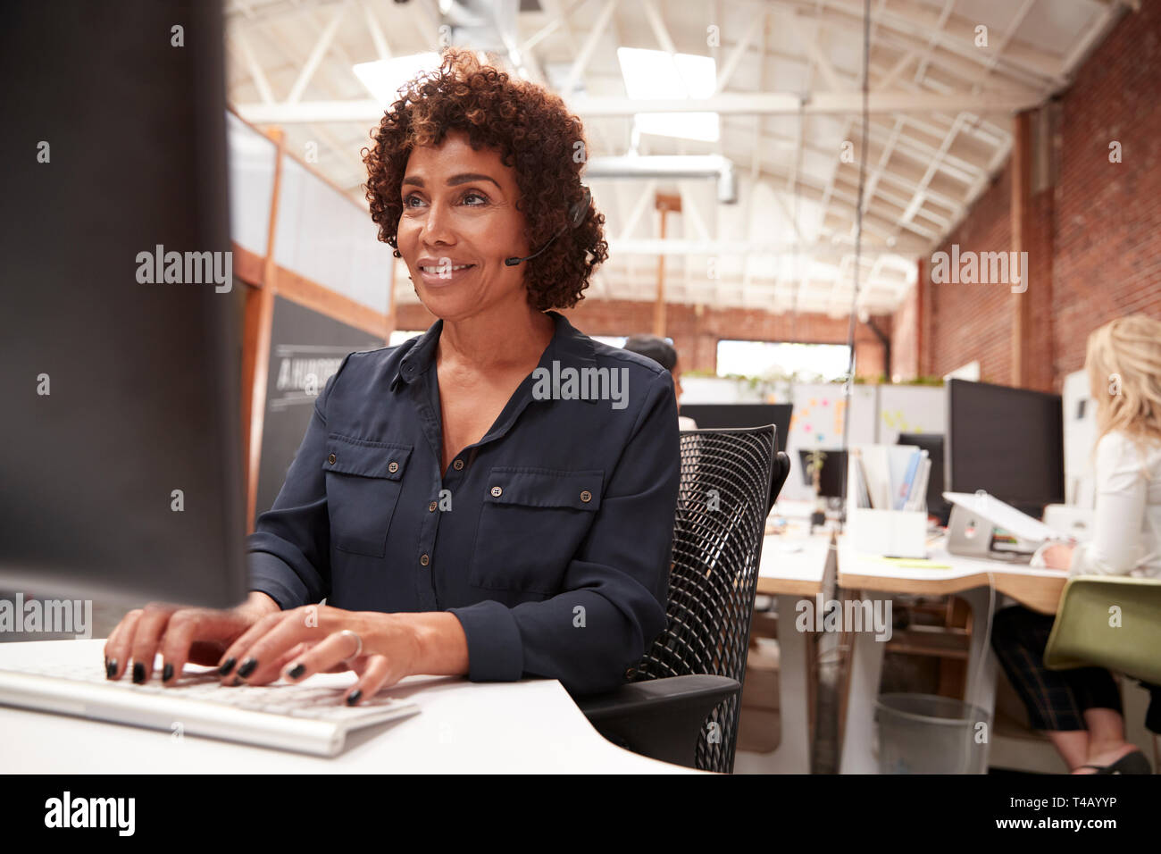 Female Customer Services Agent Working At Desk In Call Center Stock Photo